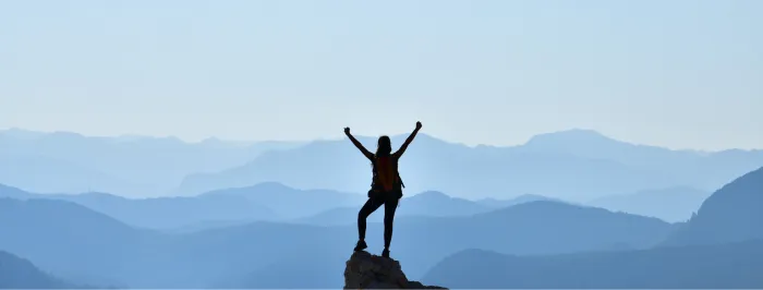 Osoba stojąca na szczycie góry z uniesionymi rękami