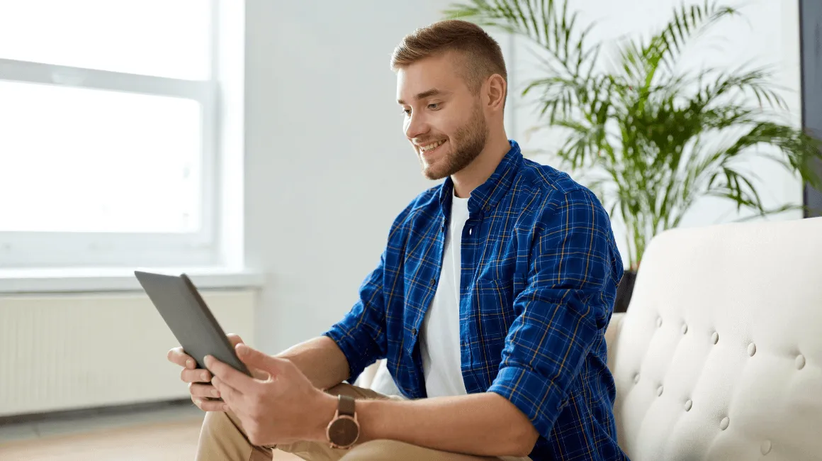 Uśmiechnięty mężczyzna siedzi na sofie i korzysta z tabletu